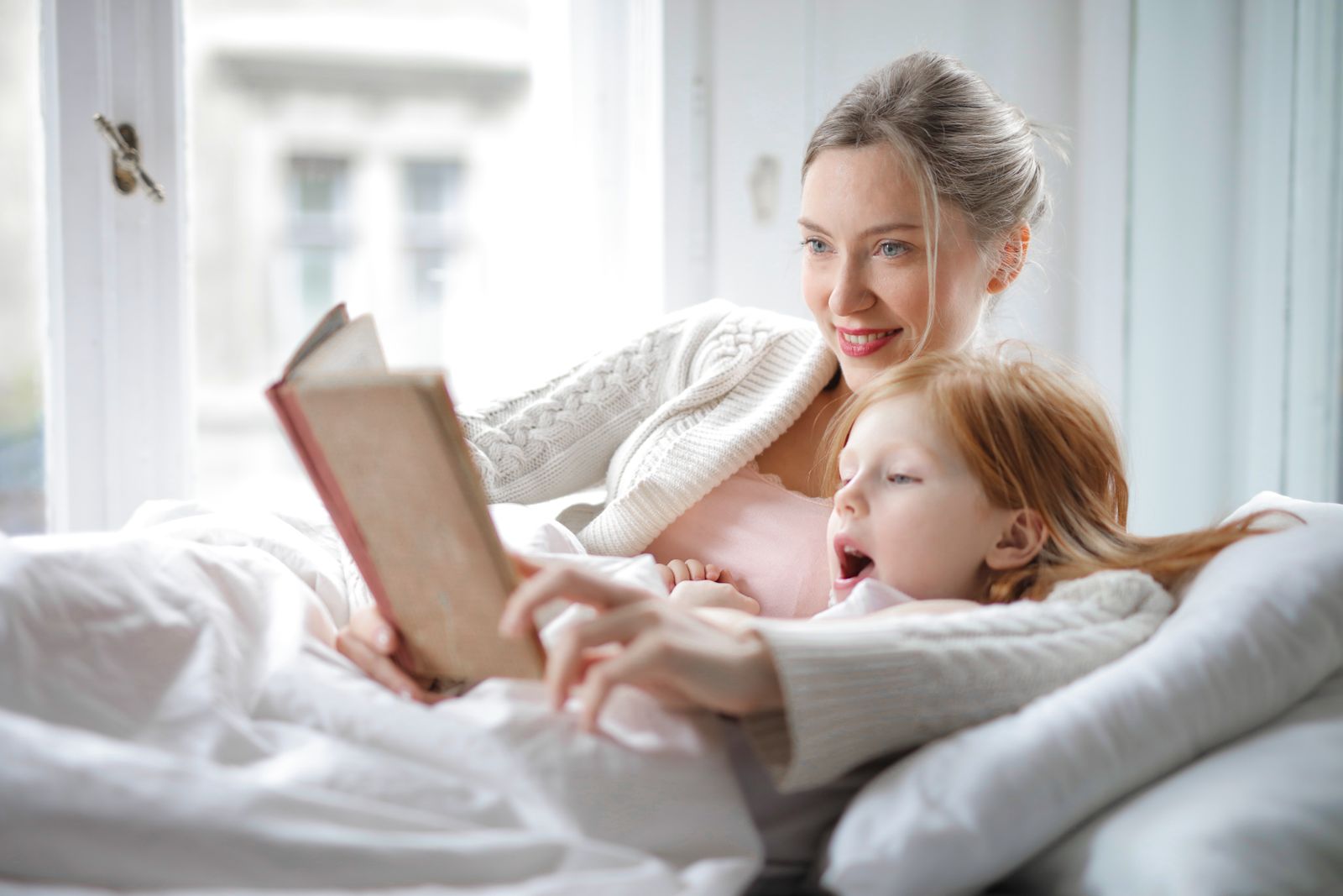 A mother and daughter reading together in bed, morning light through the window